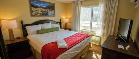 A hotel room with a bed, two bedside tables with lamps, a TV, a painting on the wall, and a window with curtains.