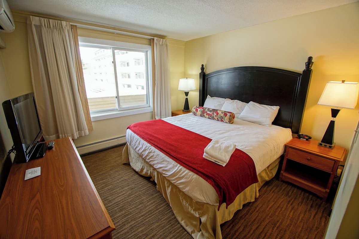 A hotel room with a bed, bedside tables, a desk, a TV, and a window with curtains.