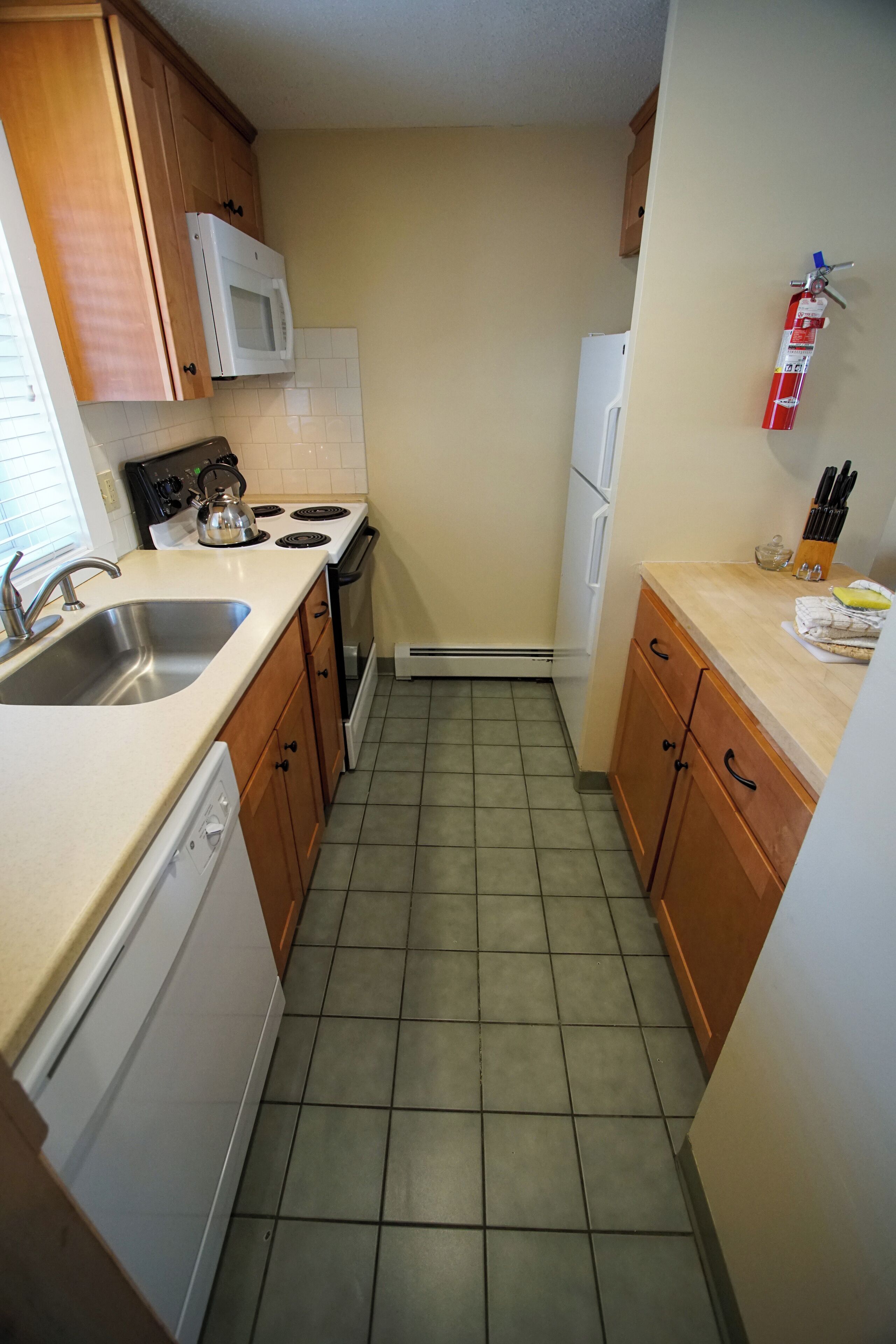 A compact kitchen with wooden cabinets, a microwave, a stove, and a sink.