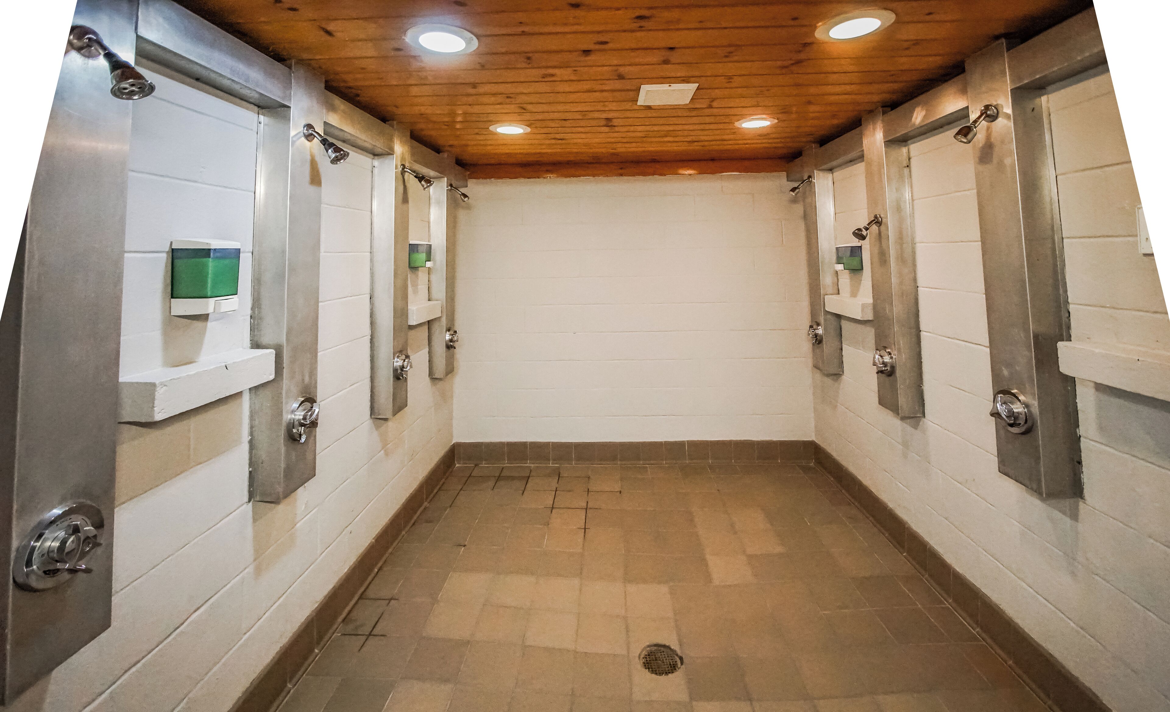 Eine öffentliche Toilette mit mehreren Kabinen, ausgestattet mit Toilette, Waschbecken und Spiegel. Die Wände sind mit Fliesen verkleidet und der Boden besteht aus Steinfliesen.