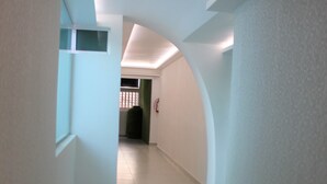 Un couloir étroit et bien éclairé, doté d’un sol carrelé et de murs blancs.