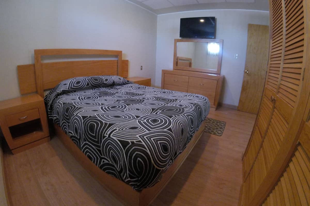 Une chambre à coucher comprenant un lit, des tables de chevet en bois, une commode, un téléviseur fixé au mur et une armoire.