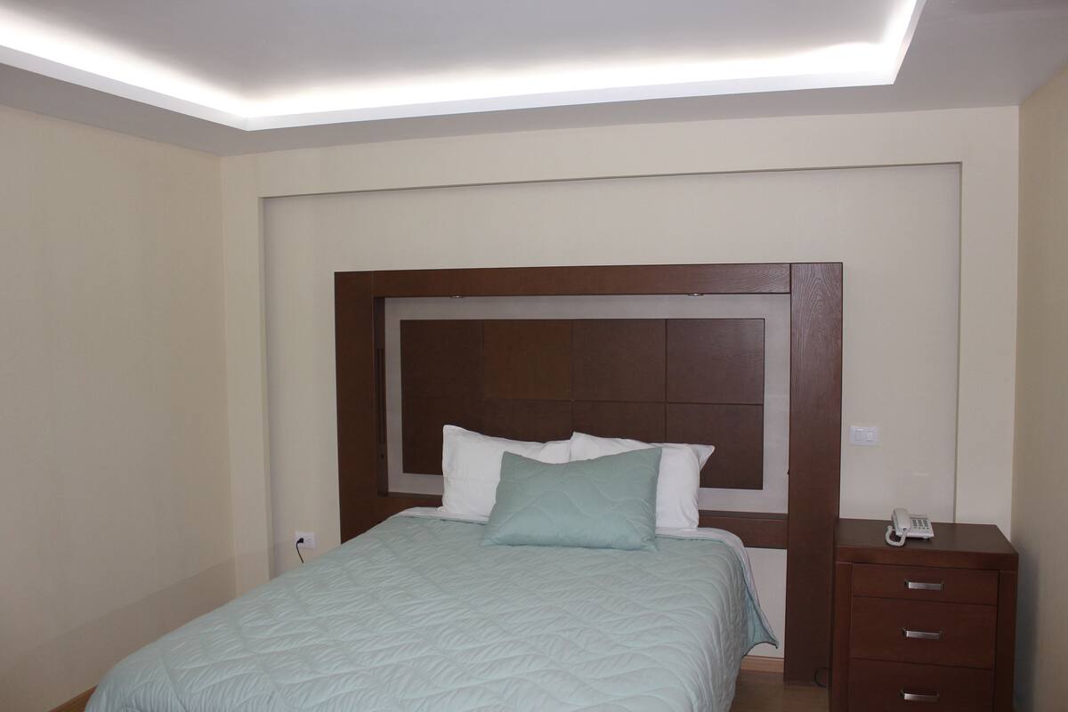 Une chambre à coucher avec un lit, une table de chevet avec un téléphone et un luminaire fixé au mur.