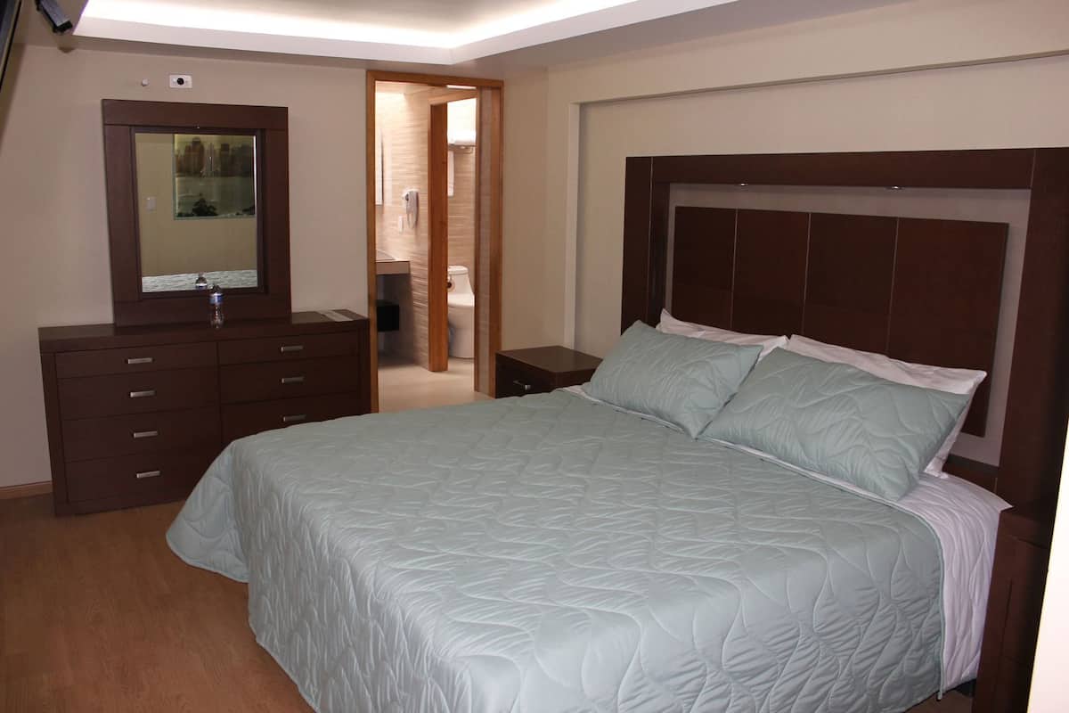 Une chambre à coucher comprenant un lit, une commode, un miroir et une porte donnant sur une salle de bain.