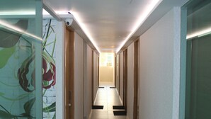 Un long couloir étroit, avec des portes en verre d’un côté, des portes en bois de l’autre, et un sol carrelé.