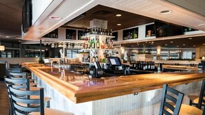 A bar area with a wooden counter, bar stools, and shelves stocked with bottles. - The Cove at Yarmouth Resort (West Yarmouth)