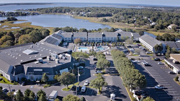 An aerial view of a hotel with a swimming pool, parking lot, and a view of a lake. - The Cove at Yarmouth Resort (West Yarmouth)