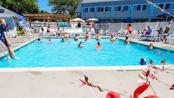Relax by the pool surrounded by lounge chairs and umbrellas, with a clear view of the surrounding trees and building.