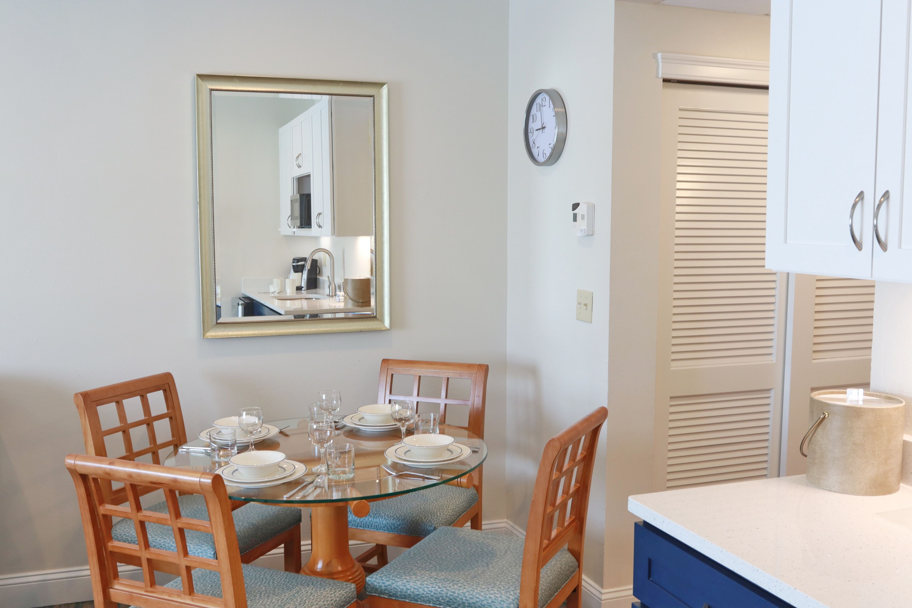 Un comedor con mesa de vidrio, sillas de madera y un espejo en la pared.