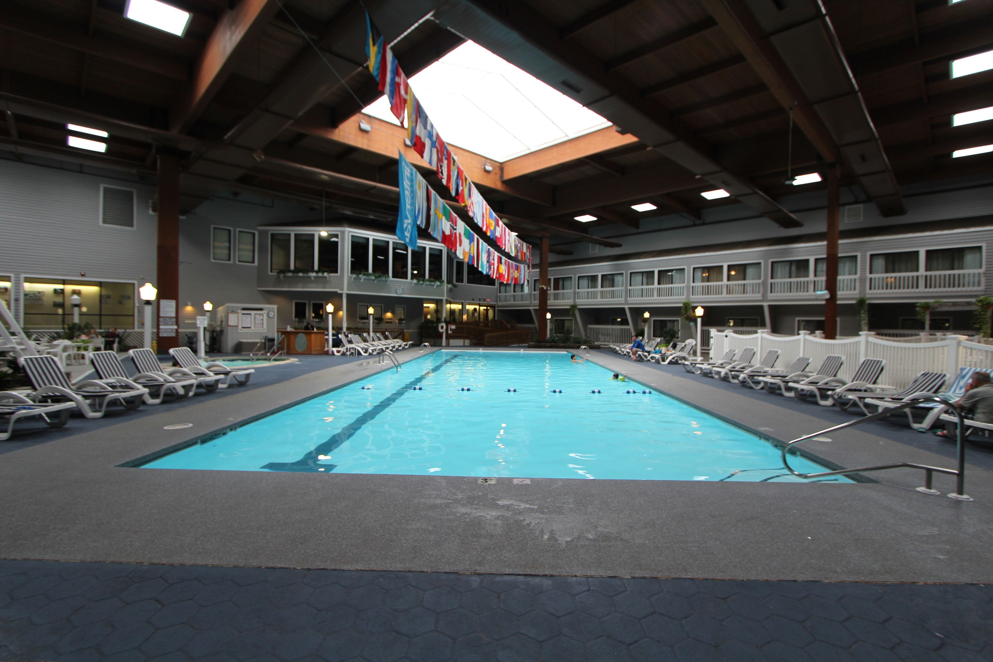 A large indoor swimming pool with multiple lounge chairs around the perimeter and a row of flags hanging from the ceiling.