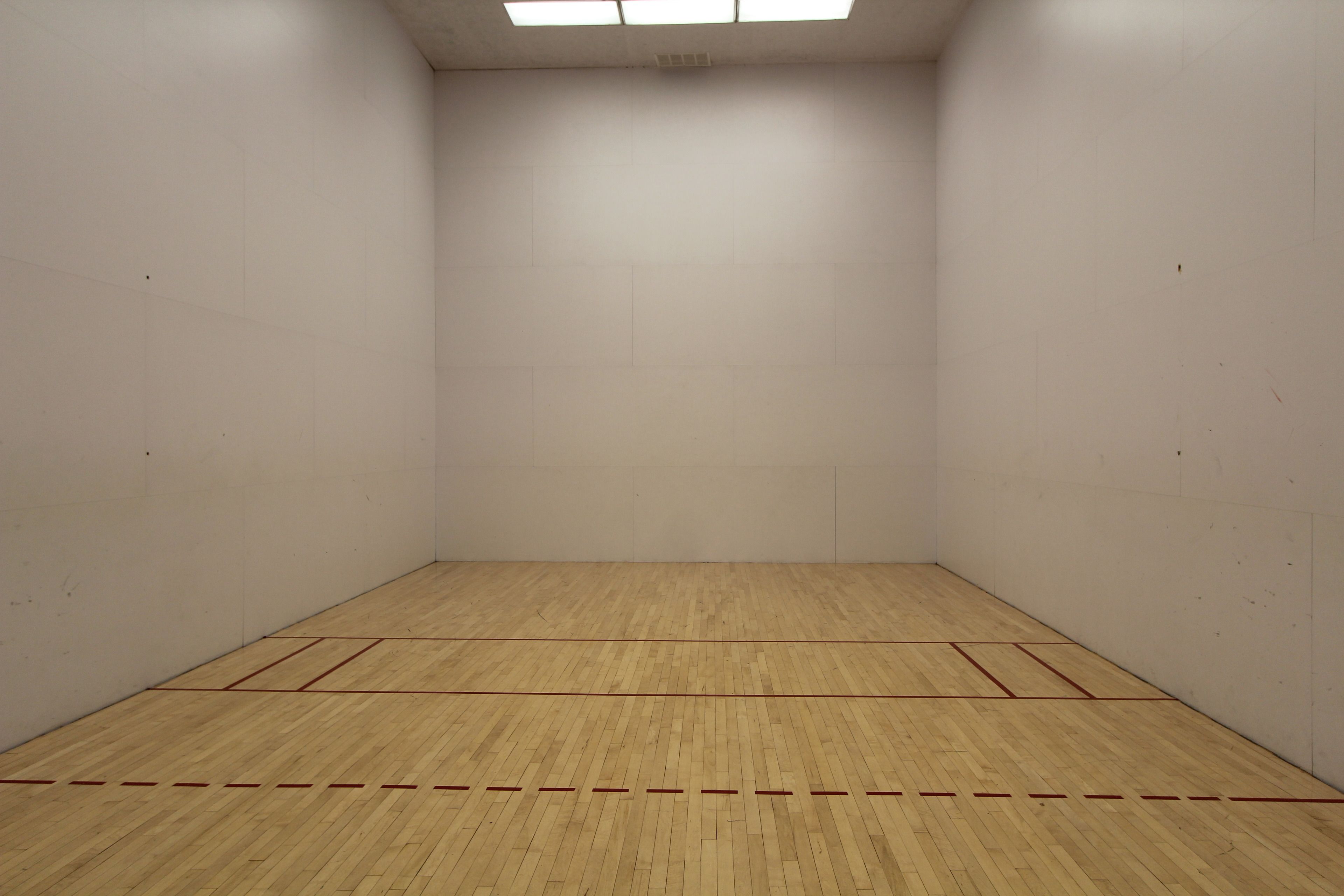Una cancha de squash con piso de madera y paredes blancas.