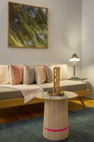 A modern living room with a wooden coffee table, a sofa with patterned cushions, a floor lamp, and a large abstract painting on the wall.