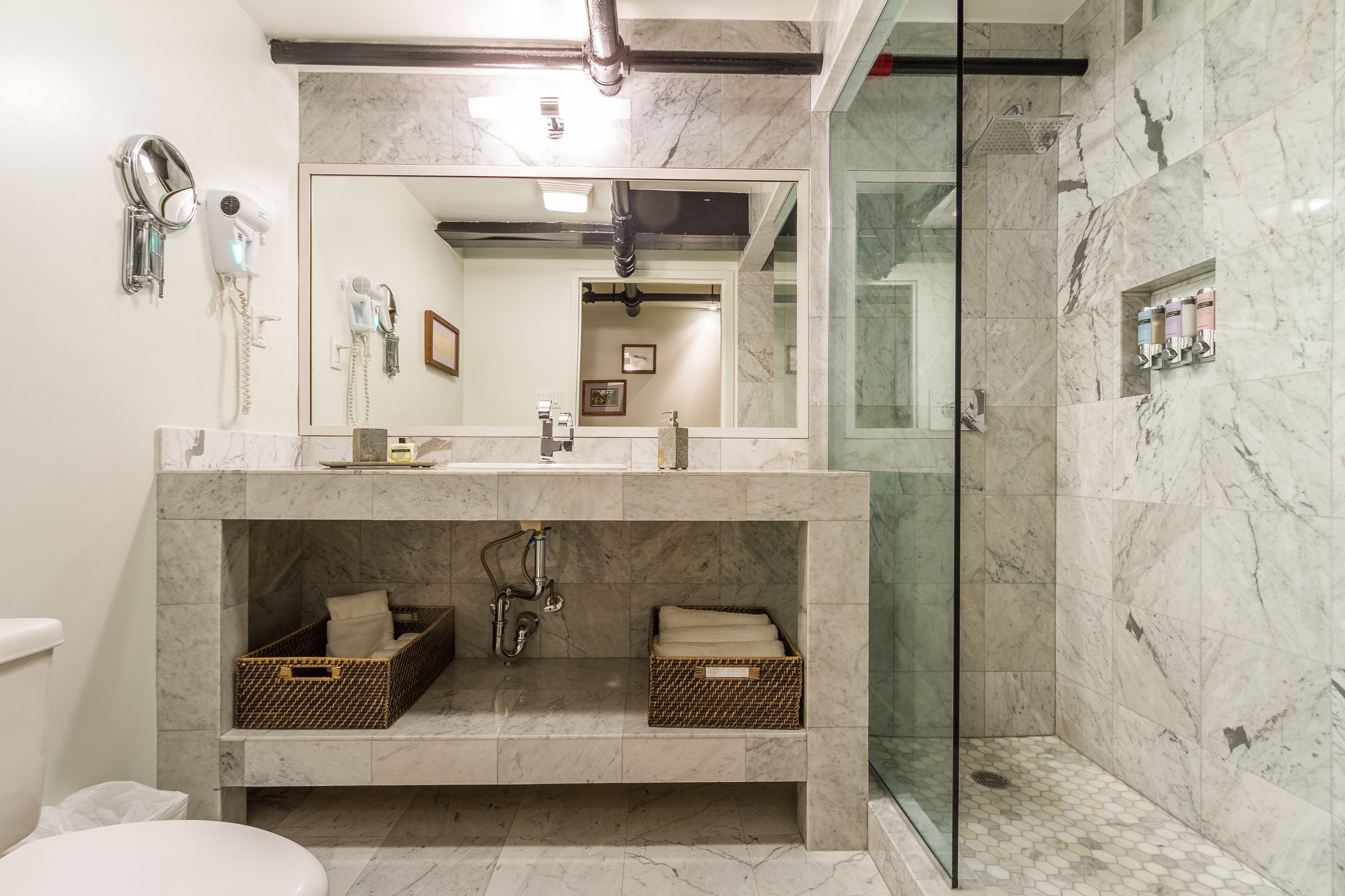 Un baño moderno con tocador de mármol, lavamanos dobles, un espejo grande, ducha con mampara de vidrio y cestas de almacenamiento.