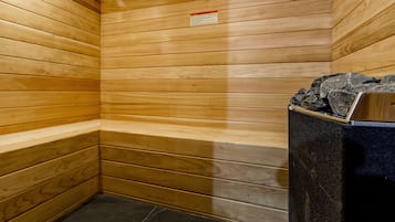 A sauna room with wooden walls, a bench, and a black heater with rocks on top.