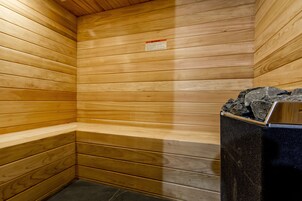 Un sauna con paredes de madera, un banco y un calentador negro con piedras arriba.