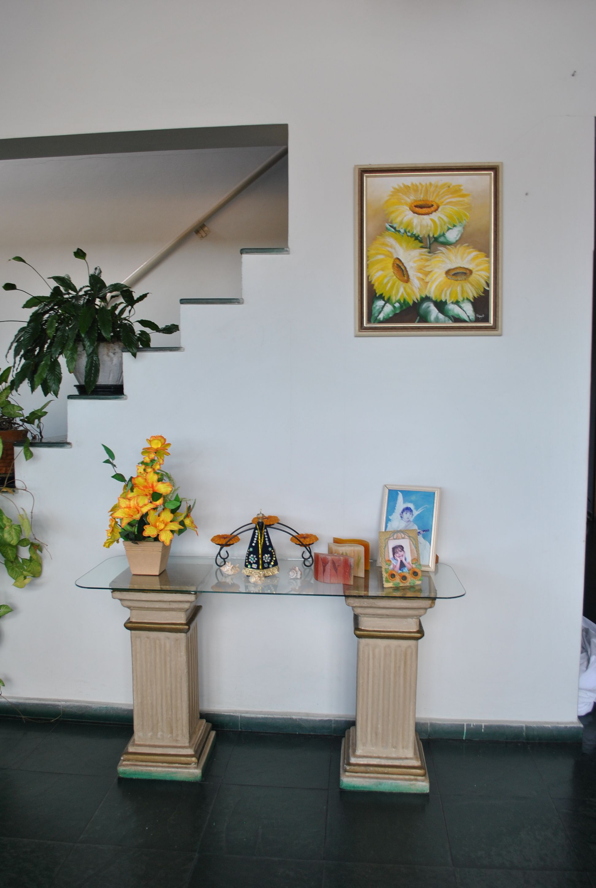 Uma área de recepção com mesa de vidro, plantas em vasos e obras de arte emolduradas.