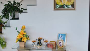 Uma área de recepção com mesa de vidro, plantas em vasos e obras de arte emolduradas.