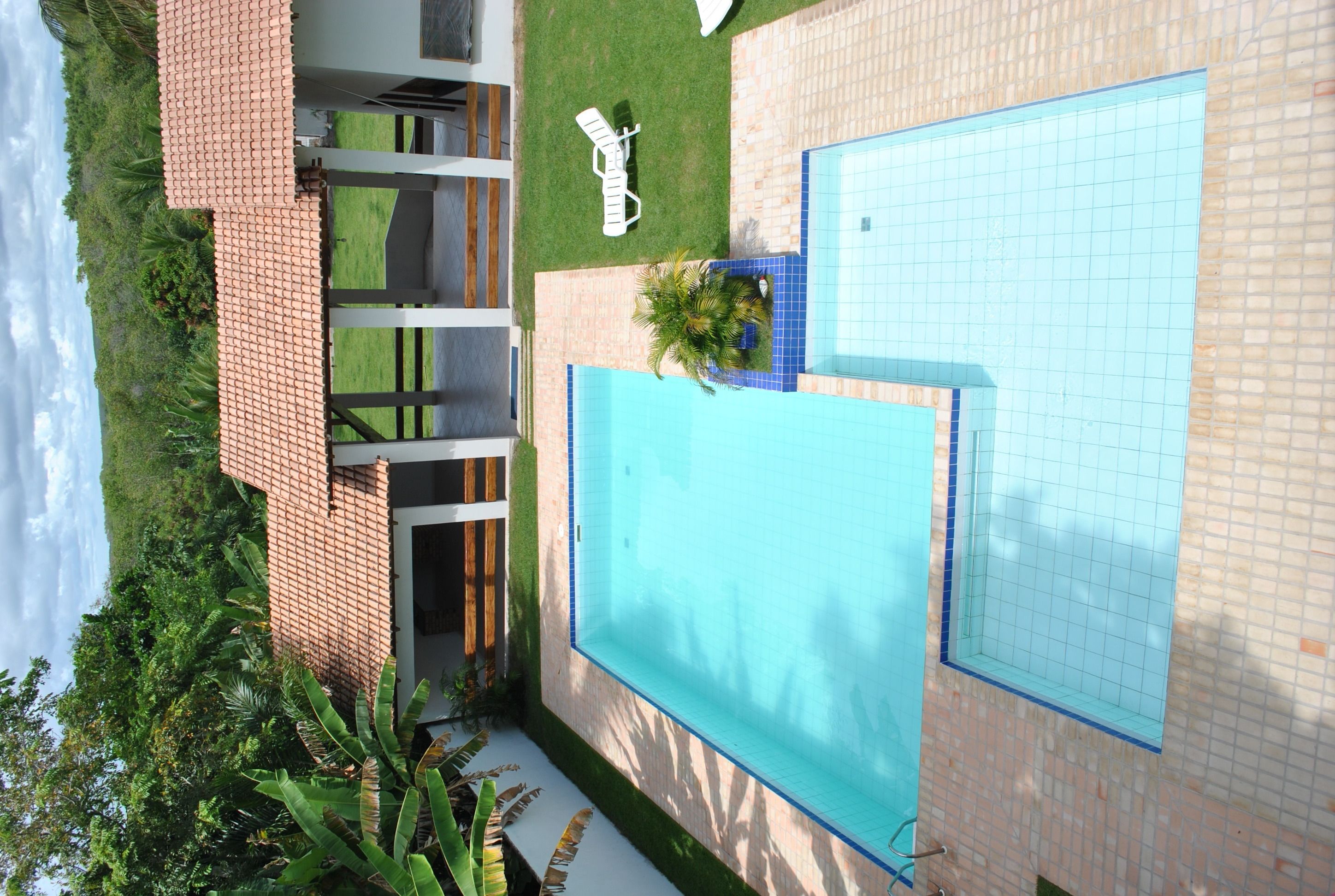 Uma piscina no terraço com vista ampla do céu, rodeada por um gramado bem cuidado e um edifício de tijolos.