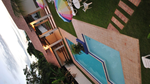 An outdoor swimming pool area with a brick deck, a pool, and several umbrellas. - Pousada Portal do Prado (Prado)