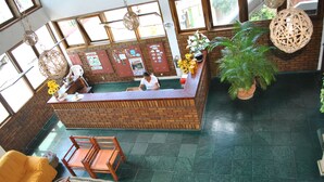 A reception area with a brick counter, wooden chairs, a large potted plant, and a yellow sofa. - Pousada Portal do Prado (Prado)