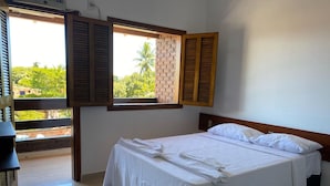 A bedroom with a bed, a window with wooden shutters, and a view of greenery outside. - Pousada Portal do Prado (Prado)