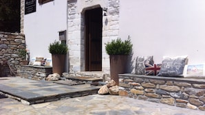 A stone-paved patio with a stone wall and a wooden door. - Mountain's Secret (Zagora-Mouresi)