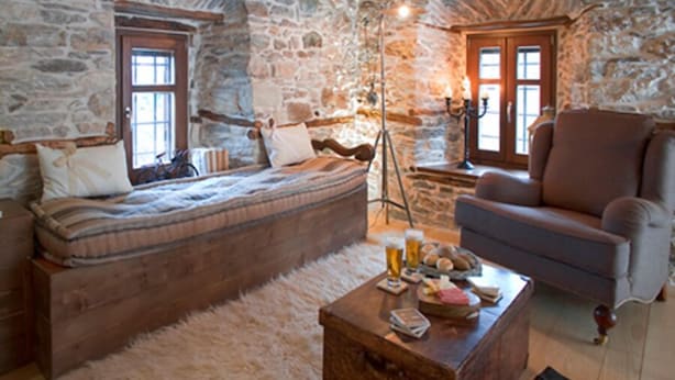A cozy room with a stone wall, a bed, a sofa, and a coffee table with drinks and snacks. - Mountain's Secret (Zagora-Mouresi)