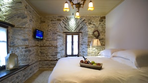 A stone-walled bedroom with a large bed, a television, and a fruit basket. - Mountain's Secret (Zagora-Mouresi)