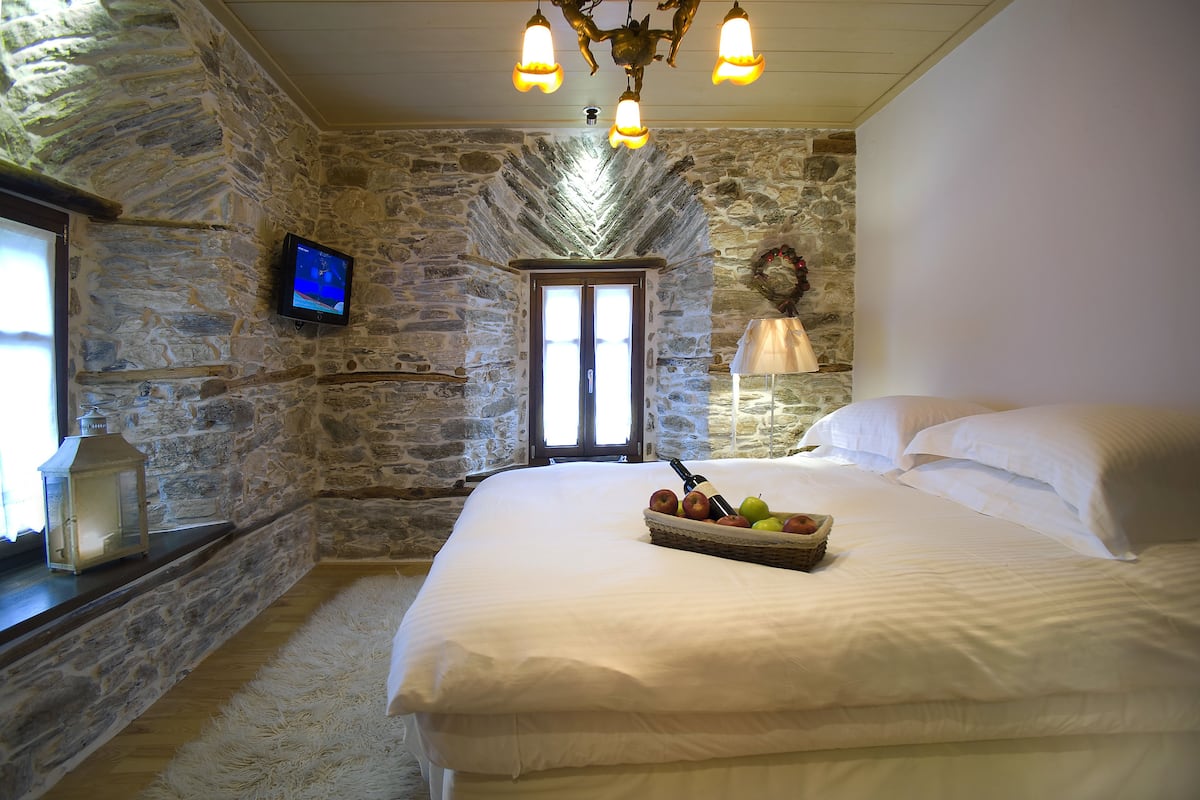 A stone-walled bedroom with a large bed, a television, and a fruit basket.