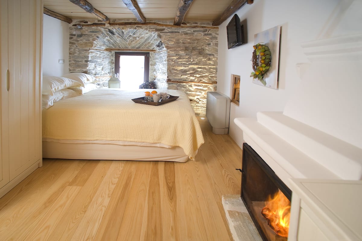 A bedroom with a stone wall, a bed with a tray of oranges and a pitcher, and a fireplace.