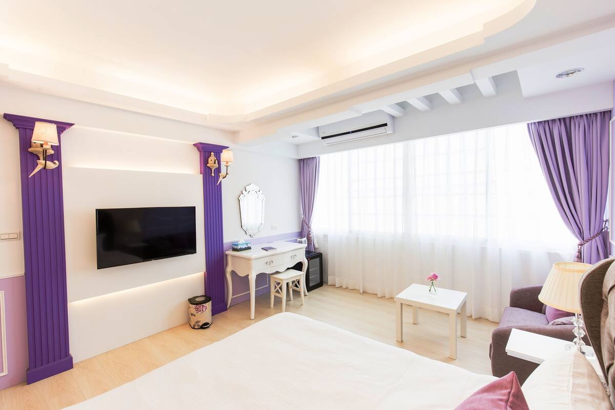 A hotel room with a bed, a desk with a chair, a television, and a small table.