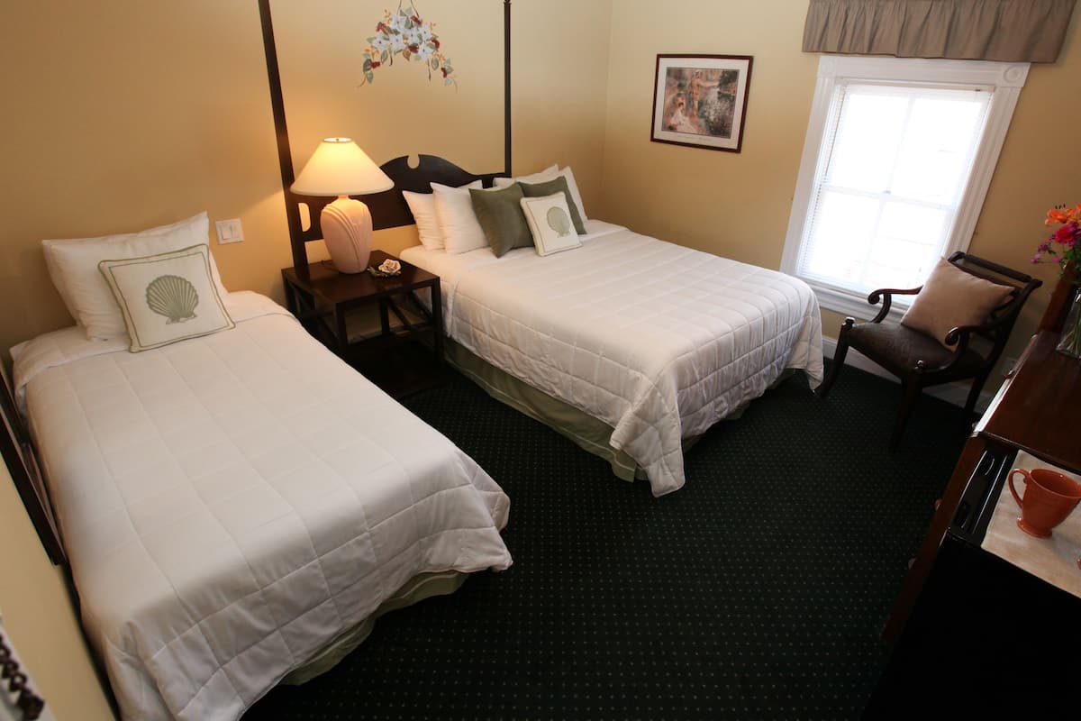 A hotel room with two single beds, a nightstand with a lamp, a chair, and a window with a view.