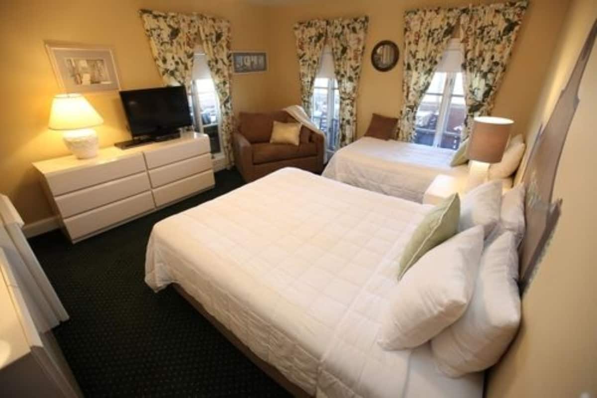 A hotel room with two beds, a TV, a dresser, and floral curtains.
