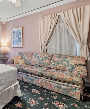 A room with a floral sofa, a bed, a lamp, a framed picture, and curtains. - The Ocean Plaza (Ocean Grove)