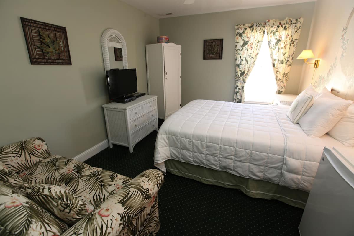 A bedroom with a bed, a dresser, a television, and a floral-patterned chair.