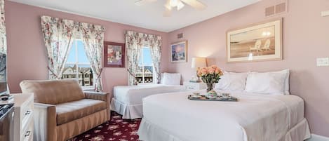 A hotel room with two beds, a sitting area with a chair, a desk, and a ceiling fan.