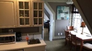 A compact kitchen with a microwave, a coffee maker, and cabinets. There is a dining area with a table and chairs, and a window providing natural light. - The Ocean Plaza (Ocean Grove)