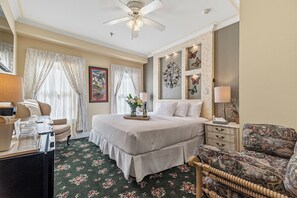 A hotel room with a bed, a desk, a chair, a ceiling fan, and decorative wall art.