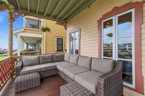 A covered porch with a sectional sofa and wicker ottomans, a balcony with a hanging flower pot, and a view of a residential area. - The Ocean Plaza (Ocean Grove)