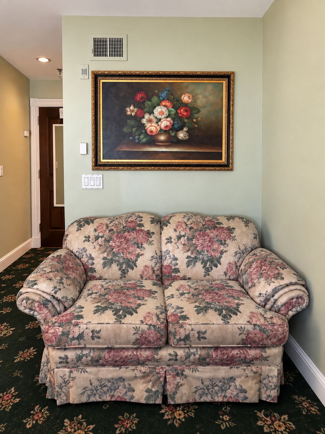 A room with a floral-patterned sofa, a painting of flowers on the wall, and a carpet with a floral design.