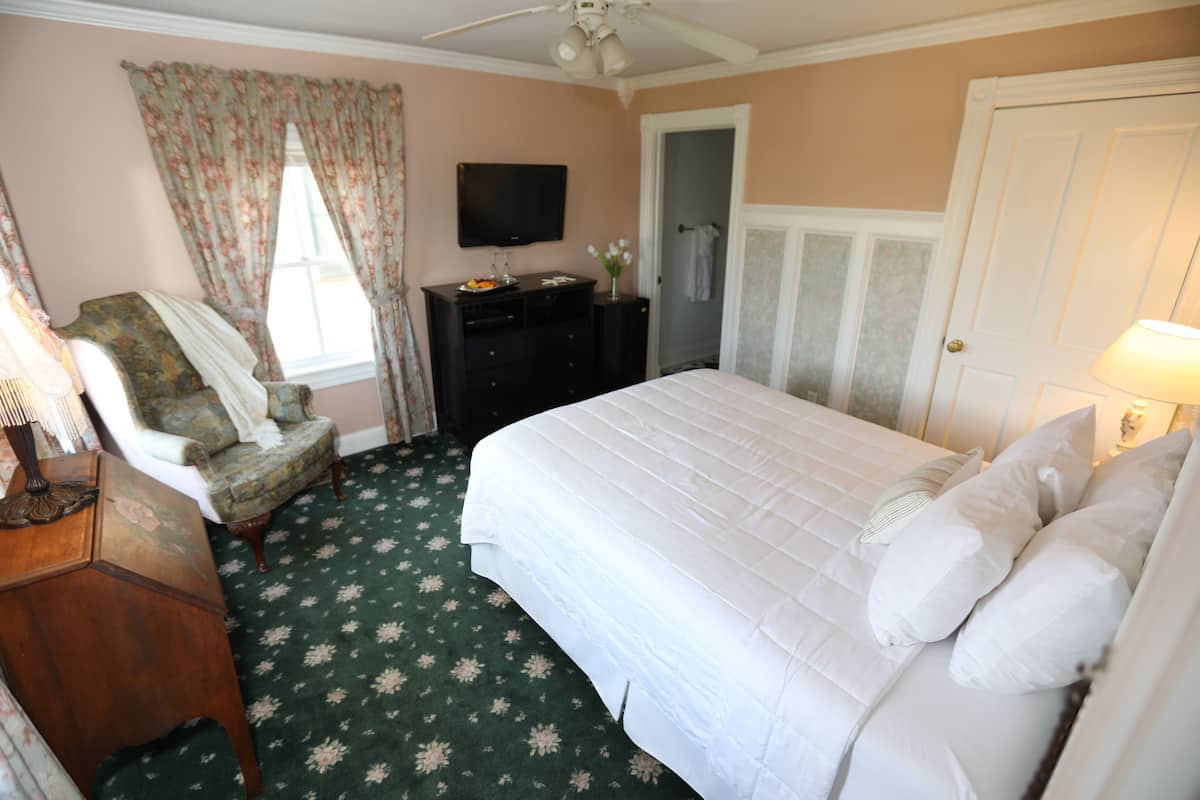 A bedroom with a bed, a chair, a dresser, a television, and a door.