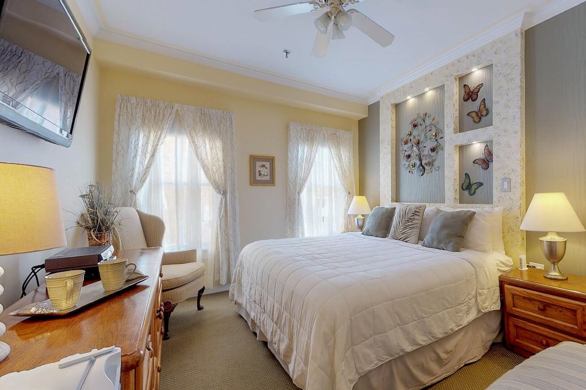 A well-lit bedroom with a bed, bedside tables, a desk, and a chair.