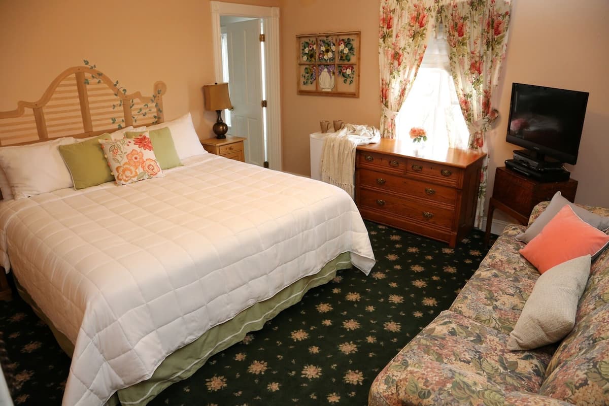 A bedroom with a large bed, a dresser, a television, and a floral-patterned sofa.