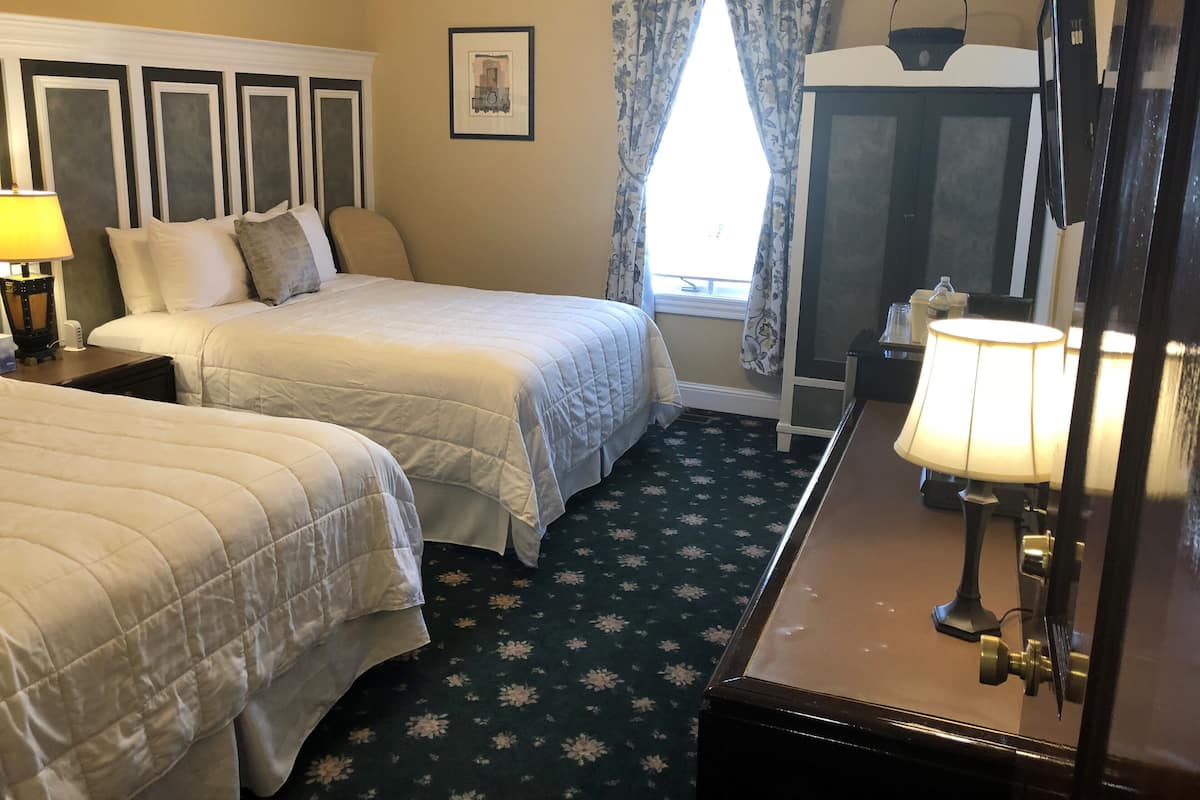 A hotel room with two beds, a large mirror, a window with floral curtains, and a carpet with a floral pattern.