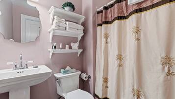 A bathroom with a white sink, a toilet, a towel rack with folded towels, and a shower curtain with palm tree designs.