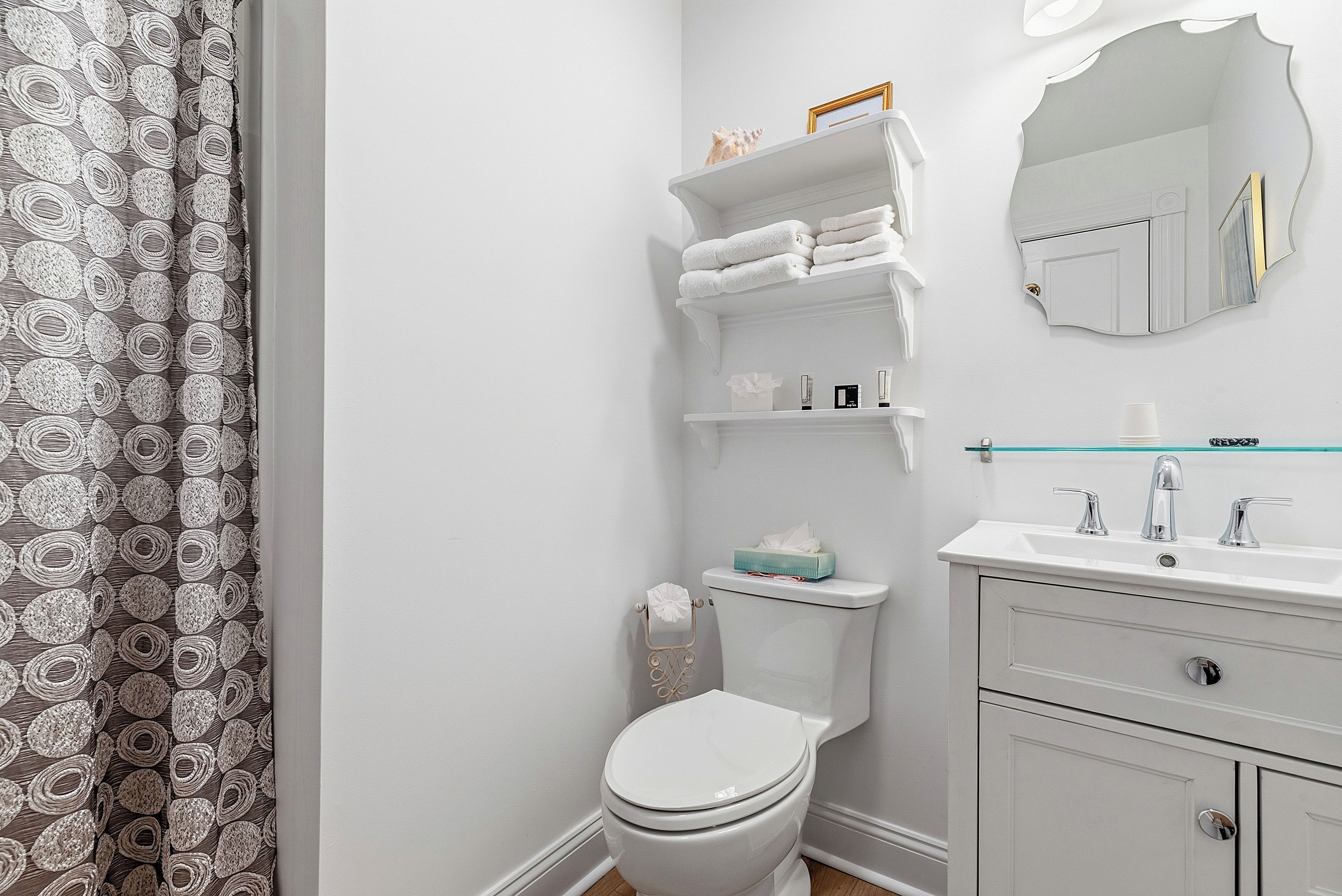 A bathroom with a toilet, a sink, a mirror, and shelves with towels.