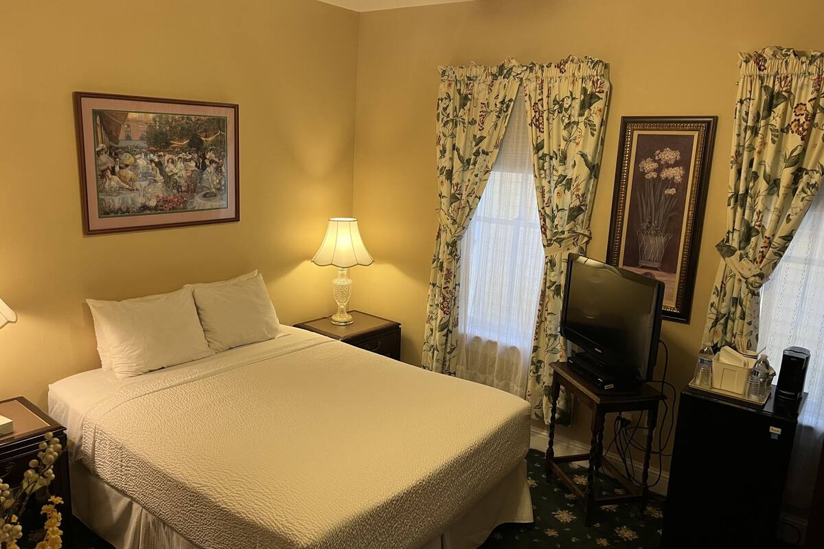 A hotel room with a large bed, a bedside lamp, a television, and floral curtains.