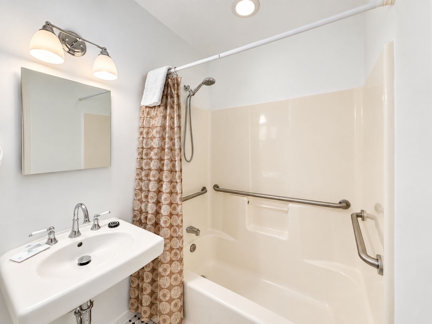 A bathroom with a white sink, a mirror, a shower with a glass door, and a towel hanging on a rack.