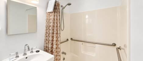 A bathroom with a white sink, a mirror, a shower with a glass door, and a towel hanging on a rack.