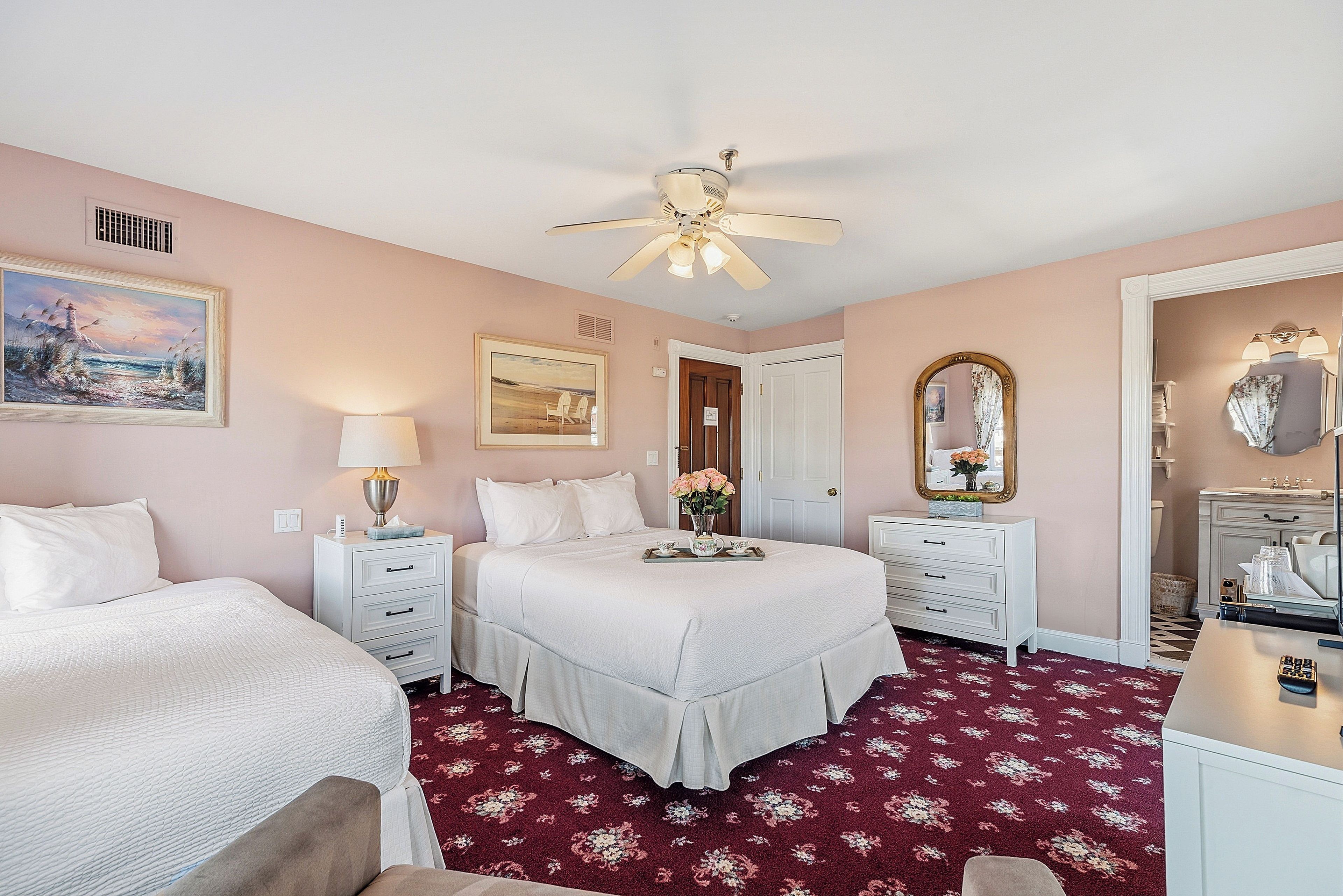 A bedroom with a bed, two bedside tables, a nightstand, a ceiling fan, a door, a mirror, and a dresser.